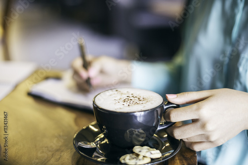 woman in holding a cup of cappuccino while writing 