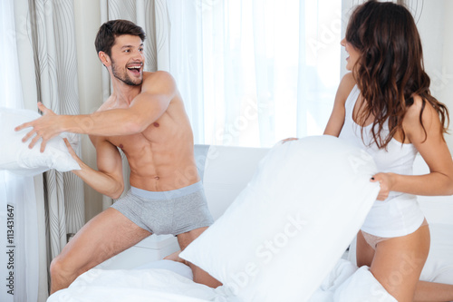 Happy couple having pillow fight in bed at bedroom