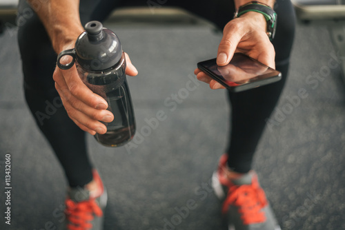 Fitness man looking to the phone for motivation before gym workout. Sporty male athlete looking his smartphone holding water bottle.