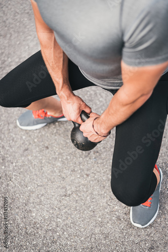 Male athlete working out legs with kettlebell. Sporty man working out outdoor on asphalt.
