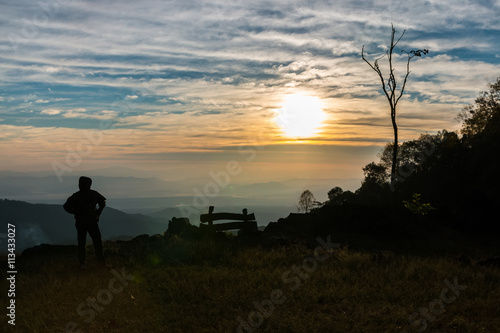 Silhouette of man is standing on top of mountain at sunrise.