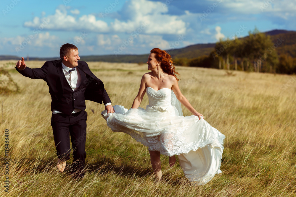 Bride whirls around her dress walking with a groom across the fi Bride whirls around her dress walking with a groom across the fi