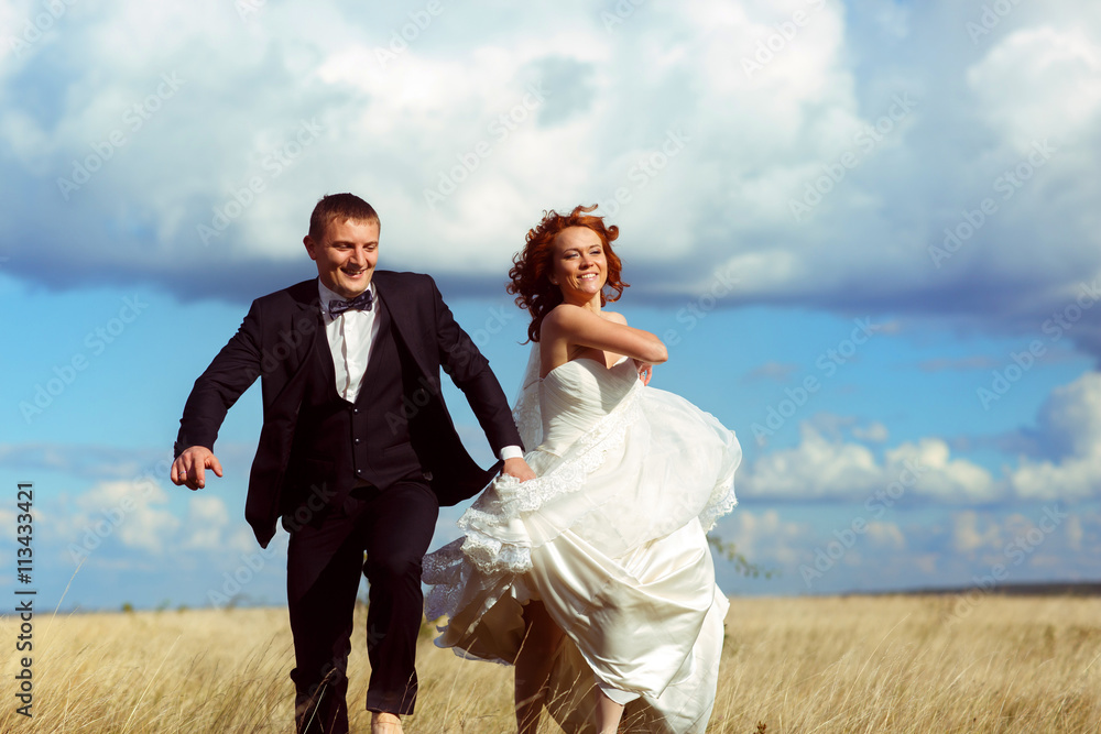 Bride rises her dress up walking across the field with a groom u Bride rises her dress up walking across the field with a groom u