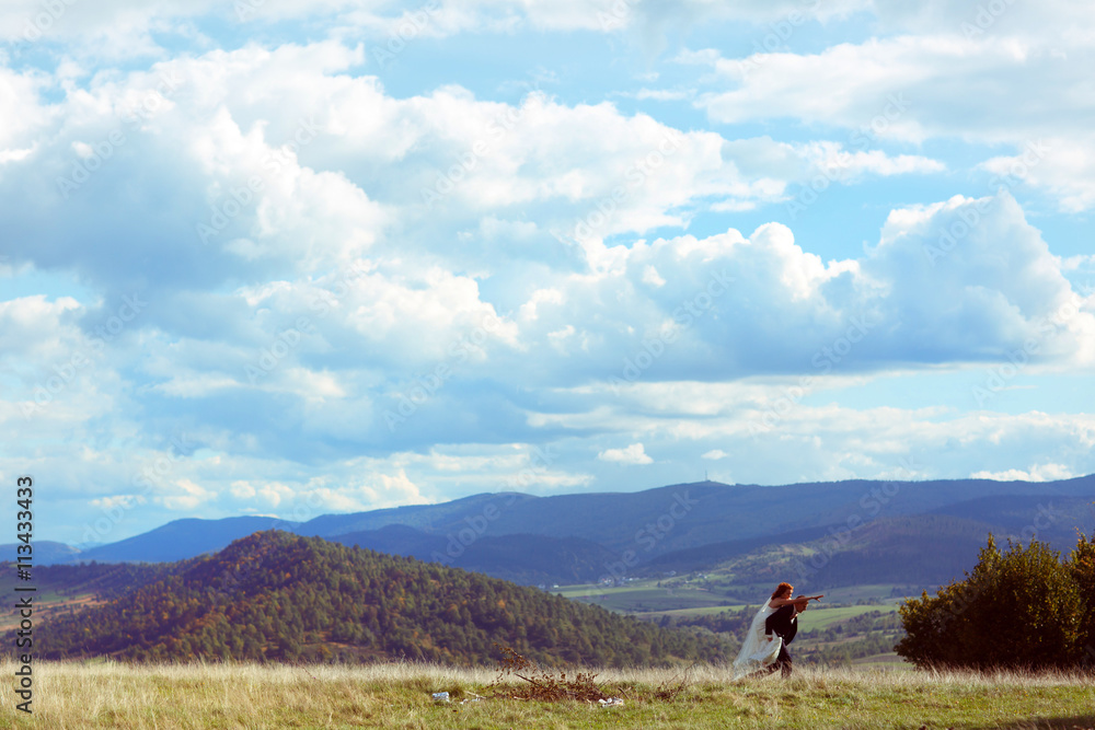 Groom bears a bride on his shoulders crossing a hill under shiny