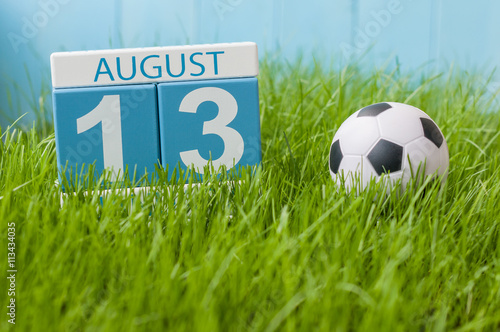 August 13th. Image of august 13 wooden color calendar on green grass lawn background with soccer ball. Summer day. Empty space for text