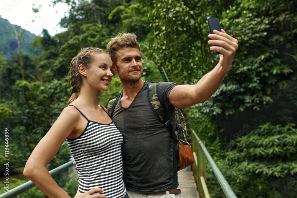 Take Photos. Couple Of Tourist People Making Selfie Photo With Mobile Phone On Summer Vacation. Beautiful Happy Friends, Man And Woman Enjoying Nature Of Tropical Forest. Travel, Tourism, Technology Take Photos. Couple Of Tourist People Making Selfie Photo With Mobile Phone On Summer Vacation. Beautiful Happy Friends, Man And Woman Enjoying Nature Of Tropical Forest. Travel, Tourism, Technology