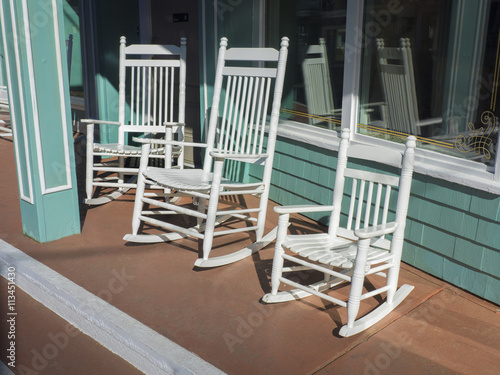 Row of hand crafted Adirondack rocking chairs on front porch of a store invite husbands to sit and chat for a short time waiting for their wives