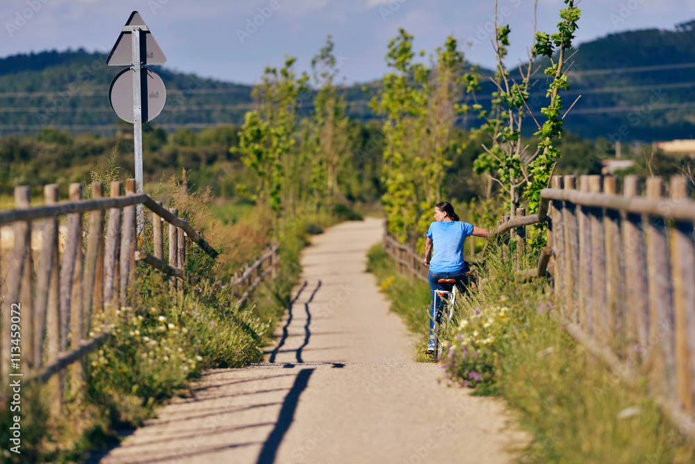 Woman on bicycle resting at fence. Old train cycling path. Bicis