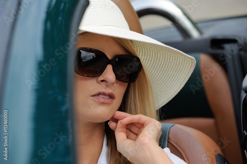 Junge Frau mit Sonnenbrille und Hut sitzt in einem Cabriolet