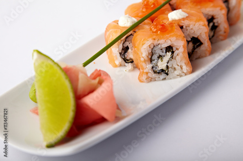 Plate of salmon sushi with lime and ginger on a white background