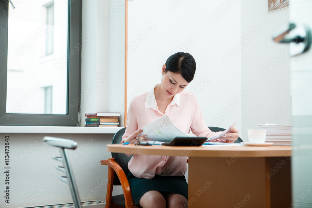 Young businesswoman sitting at workplace and reading paper in office Young businesswoman sitting at workplace and reading paper in office