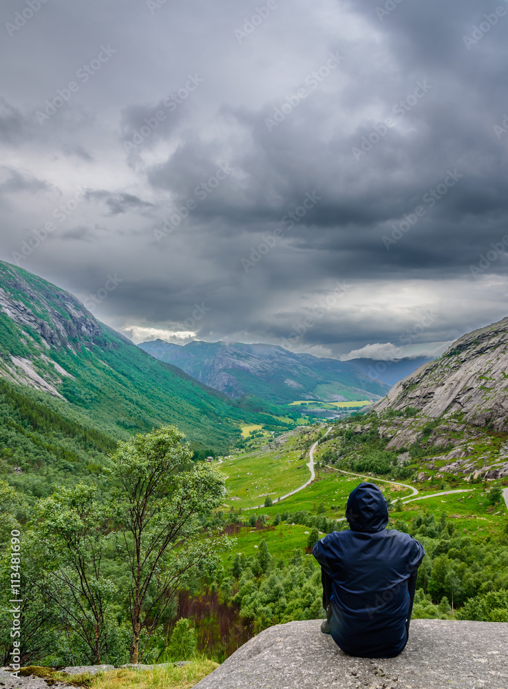 Naklejka premium Person enjoying the view over a beautiful Norwegian valley, right before the storm