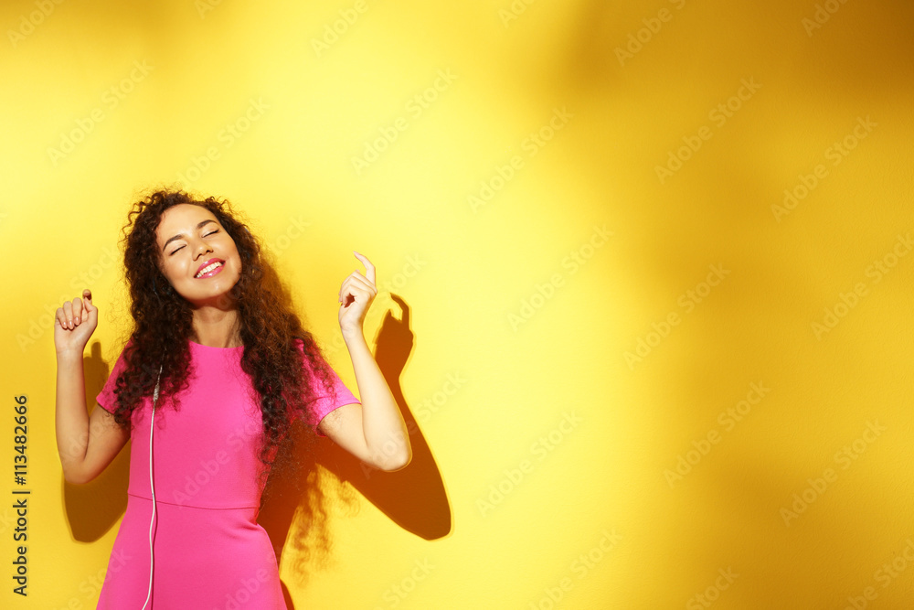African American woman listening to music in headphones on color background