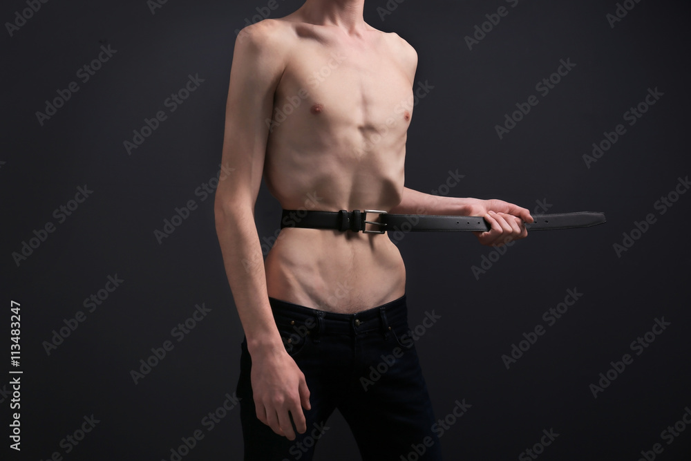 Young man tightening his waist with belt on dark background Stock Photo