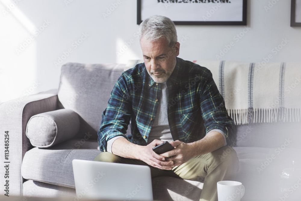Mature man using laptop while sitting on sofa at home Mature man using laptop while sitting on sofa at home