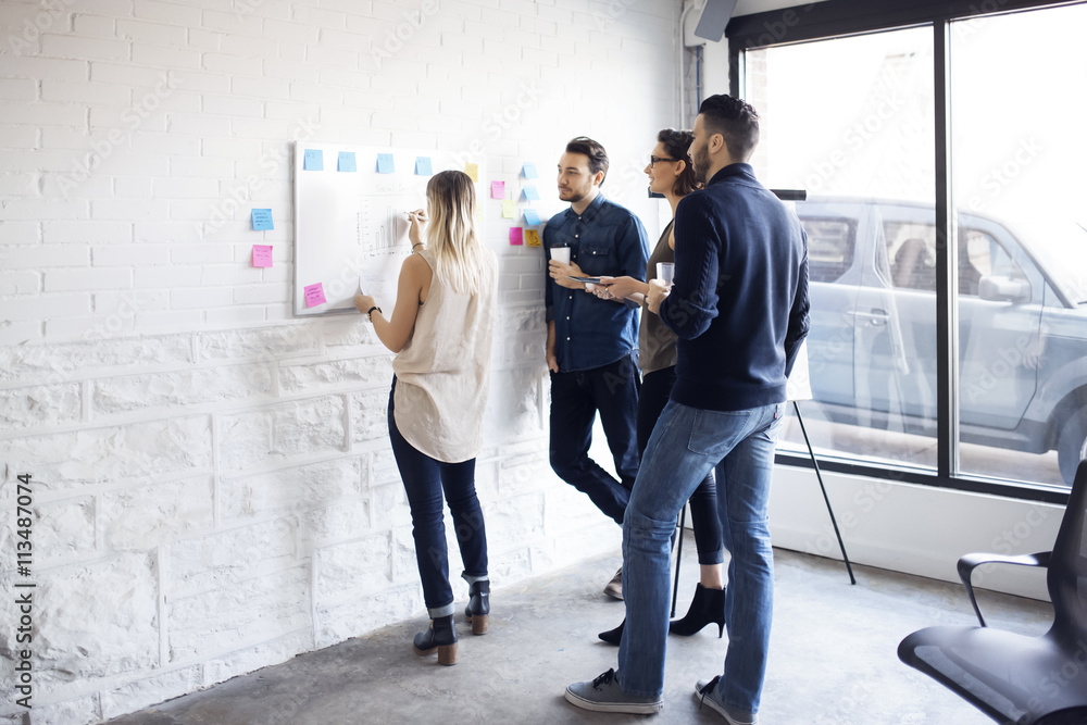 © Cavan Images - Businesswoman writing while colleagues standing by window in office