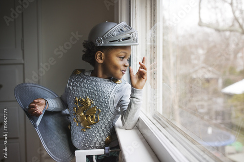 Little boy dressed up in armor costume looking out through window at home photo