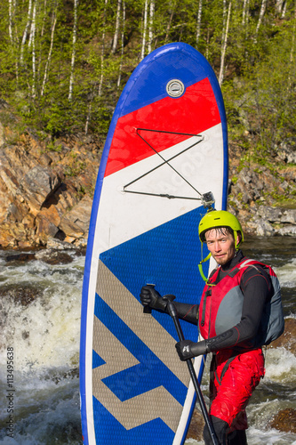 The man supsurfing on the rapids of the mountain river photo