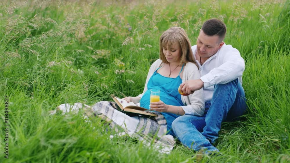 Future parents relaxing in a park. Reading a book, sitting on green grass Future parents relaxing in a park. Reading a book, sitting on green grass