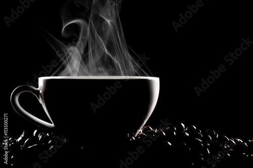 Steaming coffee cup and coffee beans in studio play of light and shadow on black background.