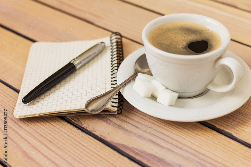 cup of coffee and a notepad with pen on wooden background cup of coffee and a notepad with pen on wooden background
