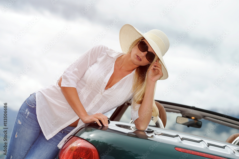 Junge blonde Frau mit Sonnenbrille, Hut und Cabrio