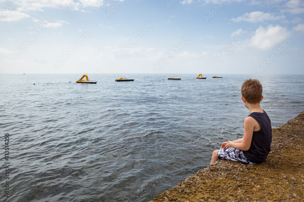 Child sitting on a pier and looking at the sea