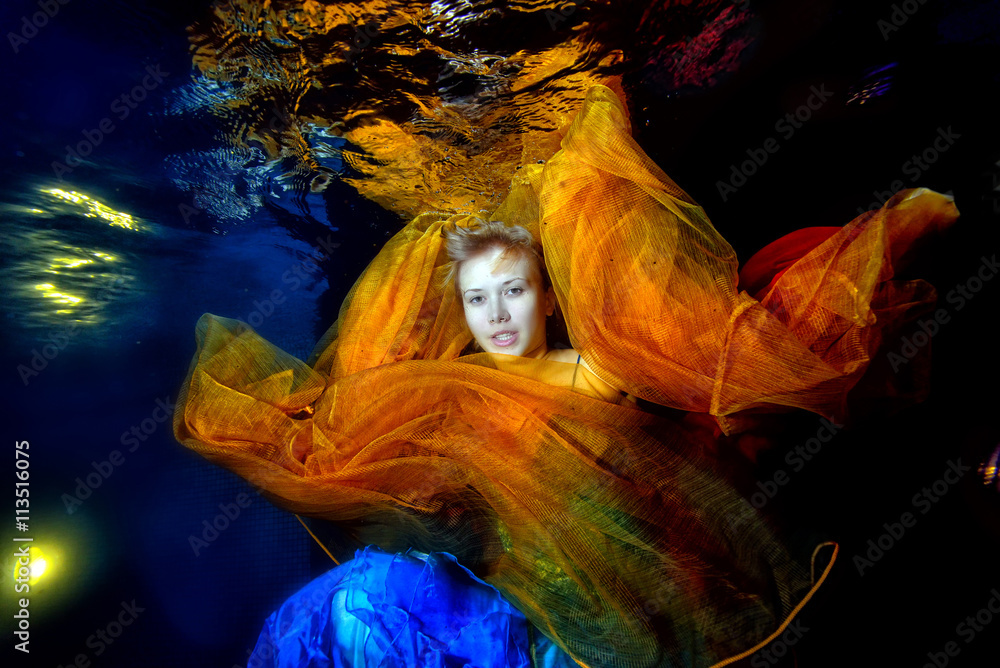 Beautiful girl posing in the pool underwater in a blue dress with an
