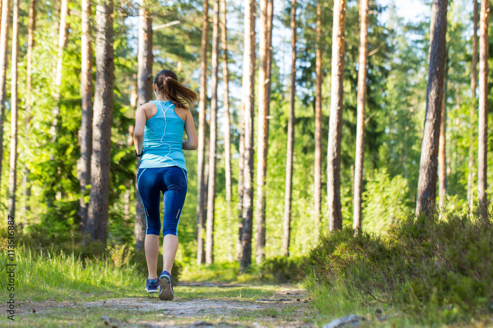 Young fitness woman running in forest trail.