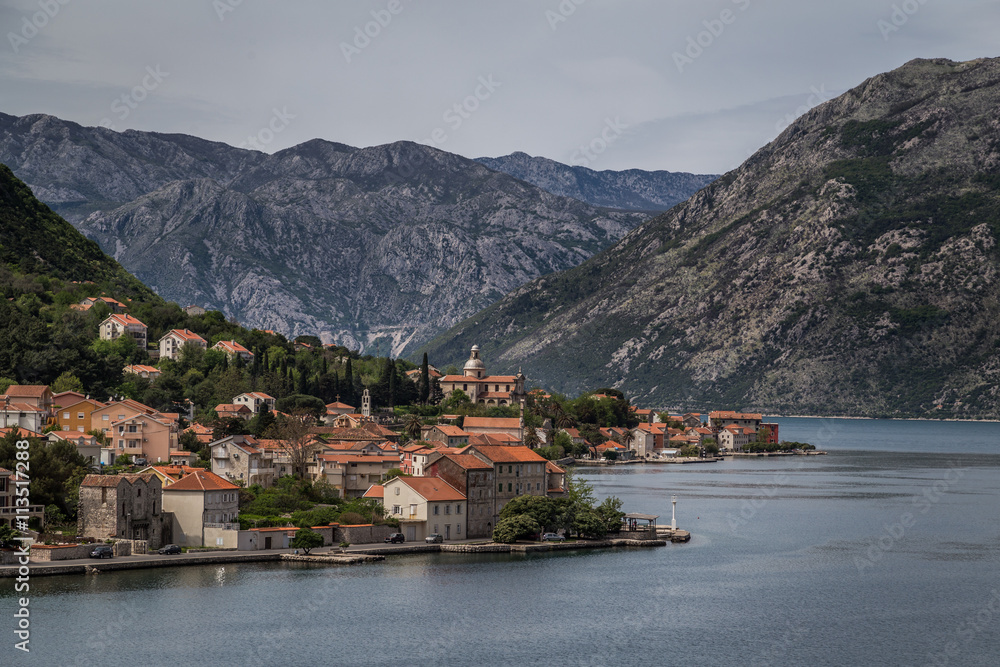 A red roofed village with a church with mountains in the background, along a mediterranean Fjord, near Kotor, Montenegro