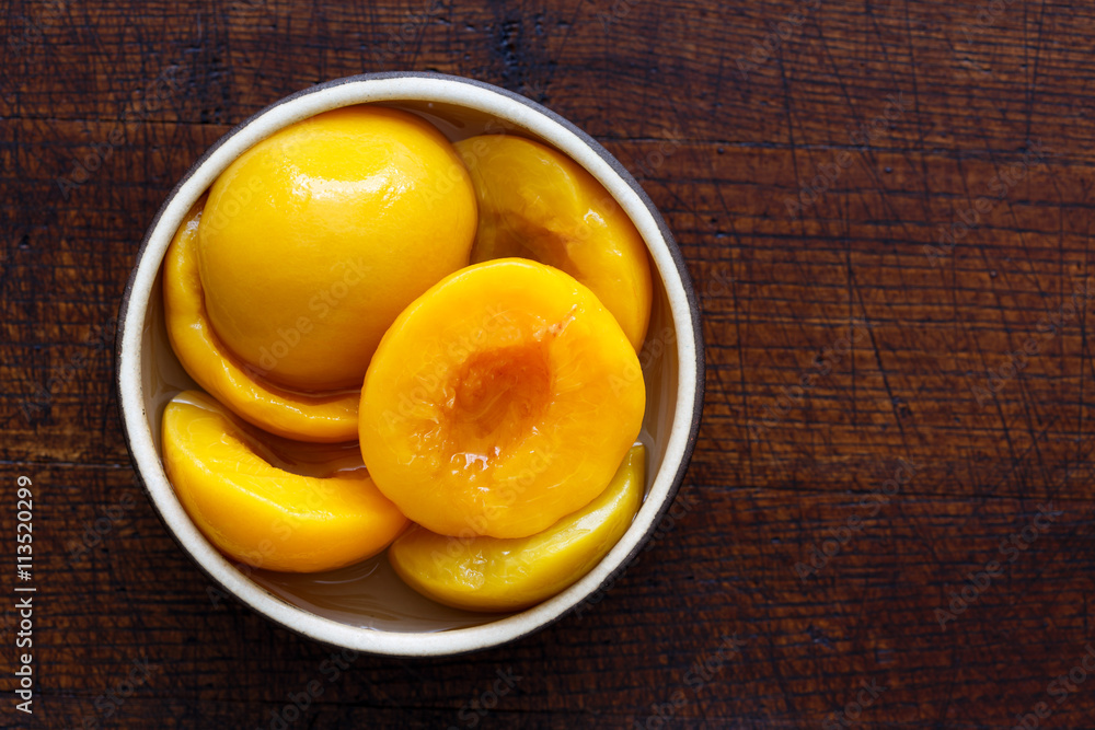 Canned peach halves in bowl isolated on dark background. From ab