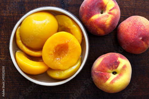Canned peach halves in bowl on dark background with whole fresh