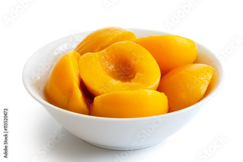 Canned peach halves in bowl isolated on white background. In per