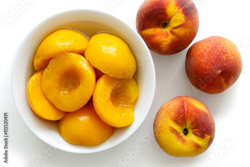 Canned peach halves in bowl on white background with whole fresh