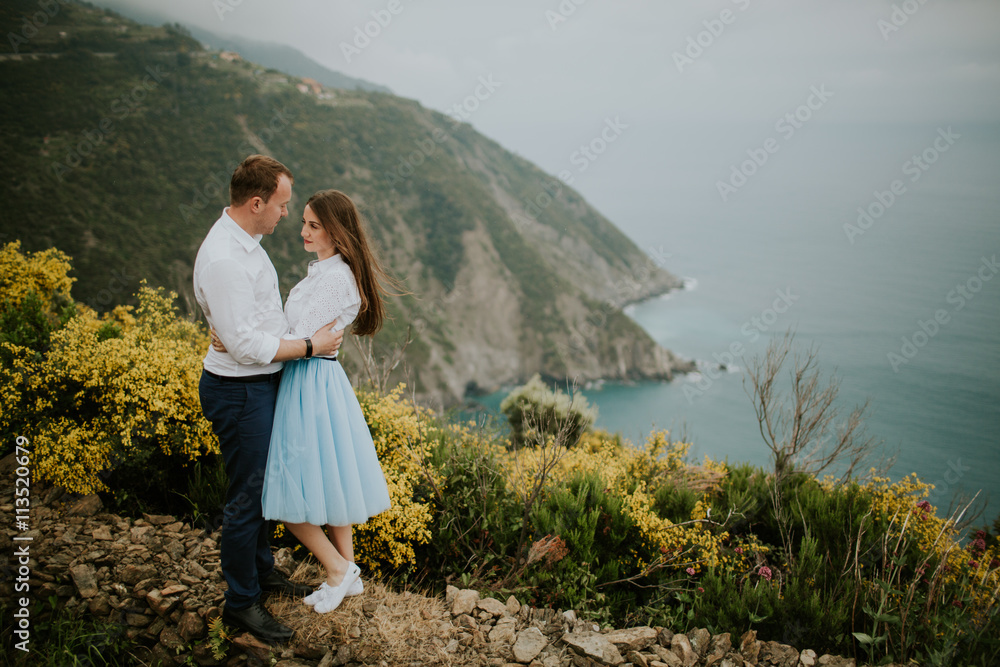 Young cute couple honeymoon walks holding their hands on dating in a beautiful place italy near ocean and mountains, hug, smile and talk to each other
