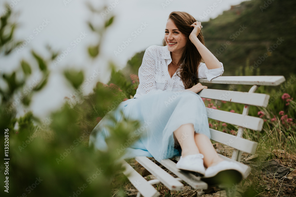 Naklejka premium Young cute smiling lady posing on a white chair in a beautiful place italy near ocean and mountains