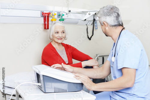 Senior Patient Looking At Male Physiotherapist Using Machine