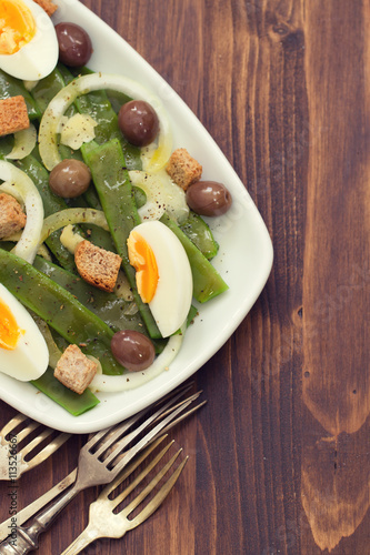 salad green beans with olives and croutins on white dish on brown wooden background