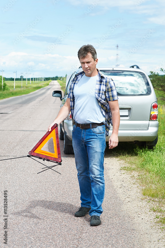 Man installing emergency sign on road near his car Man installing emergency sign on road near his car