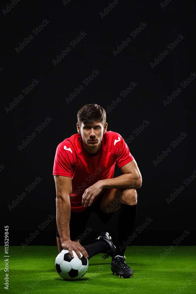 Soccer player with ball standing on one knee over black backgrou Soccer player with ball standing on one knee over black backgrou