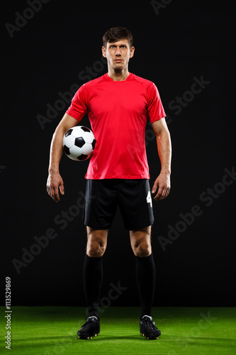 Soccer player with ball standing over black background © Cookie Studio