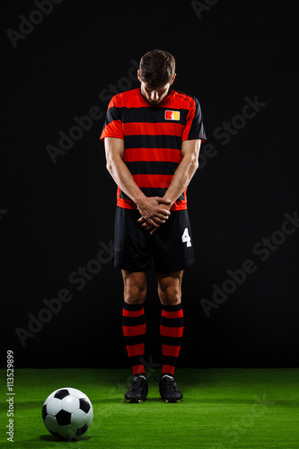 Soccer player with ball standing over black background © Cookie Studio