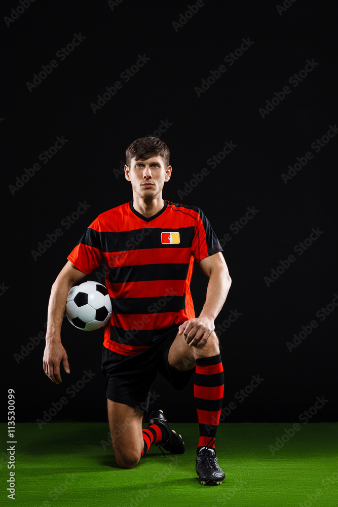 Soccer player with ball standing on one knee over black backgrou