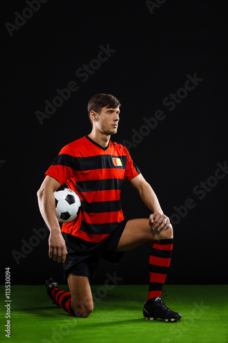 Soccer player with ball standing on one knee over black backgrou © Cookie Studio