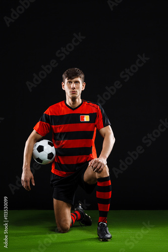 Soccer player with ball standing on one knee over black backgrou © Cookie Studio