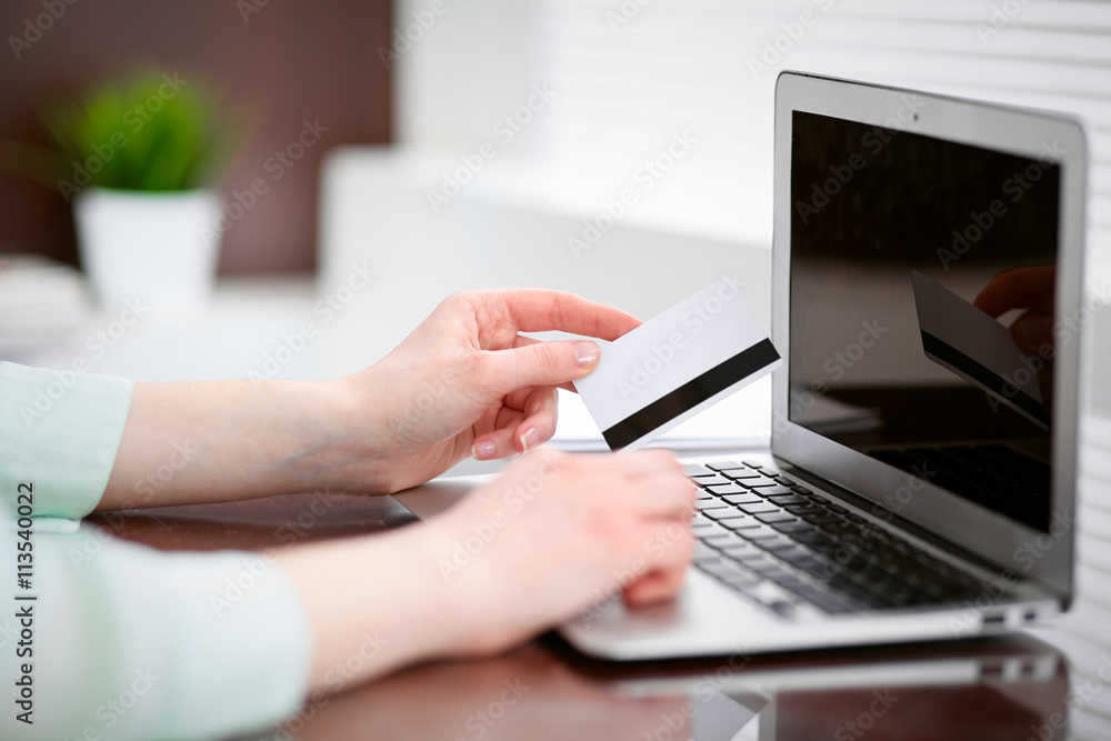 Business woman in a green blouse sitting at the desk in the office and working on laptop computer with a credit card in her hands . Business woman in a green blouse sitting at the desk in the office and working on laptop computer with a credit card in her hands .