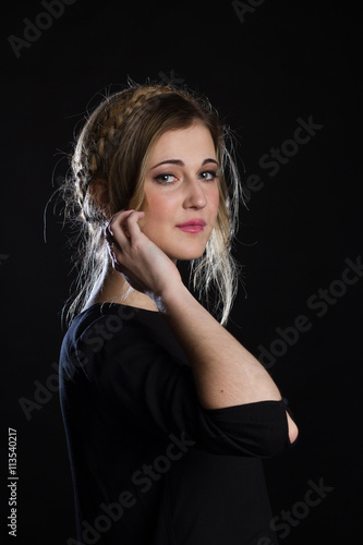 Beautiful blond girl with blue-green eyes on a black background. She wears a black t-shirt. 