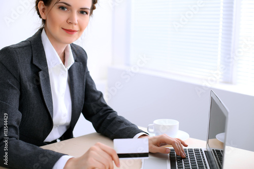 Business woman looks like yulia tymoshenko is sitting at the table and working in  white colored office . Ukrainian hair styling. Independence and success concept. photo