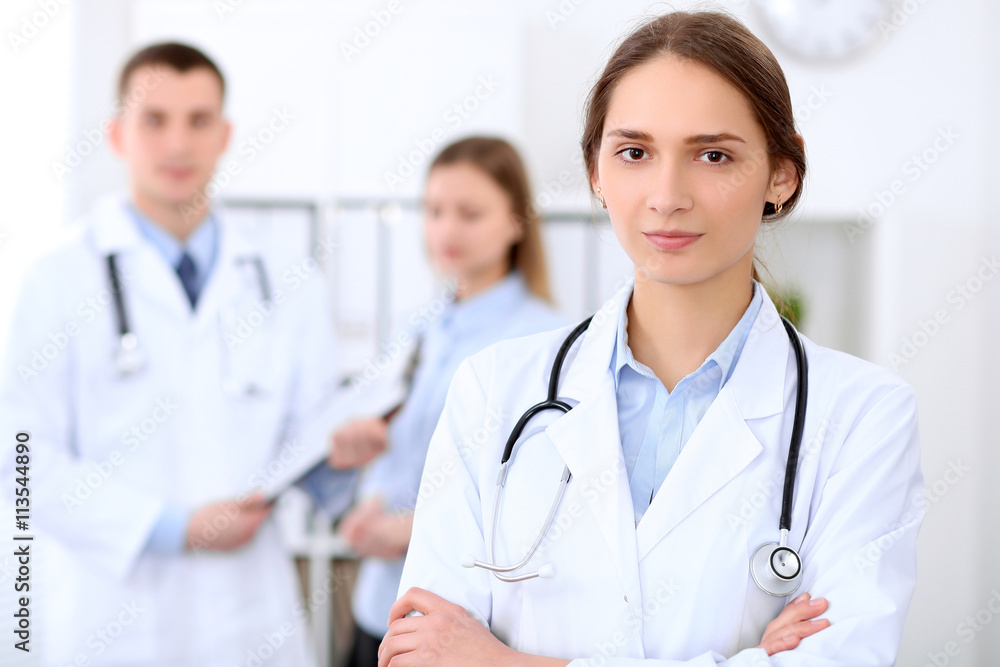 Young beautiful female doctor smiling on the background with patient and his doctor in hospital. High level and quality medical service concept. Young beautiful female doctor smiling on the background with patient and his doctor in hospital. High level and quality medical service concept.