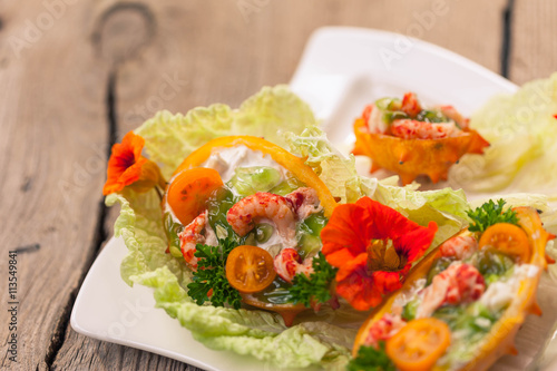 Exotic Shrimp salad served in n half a kiwano and leaves of the Chinese cabbage for summer party on wooden table, selective focus, copy space
